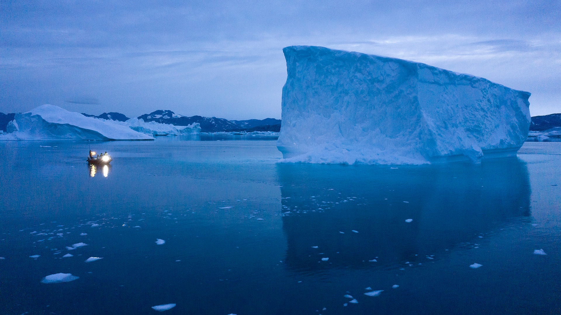 Ein kleines Boot fährt neben einem Eisberg in Grönland