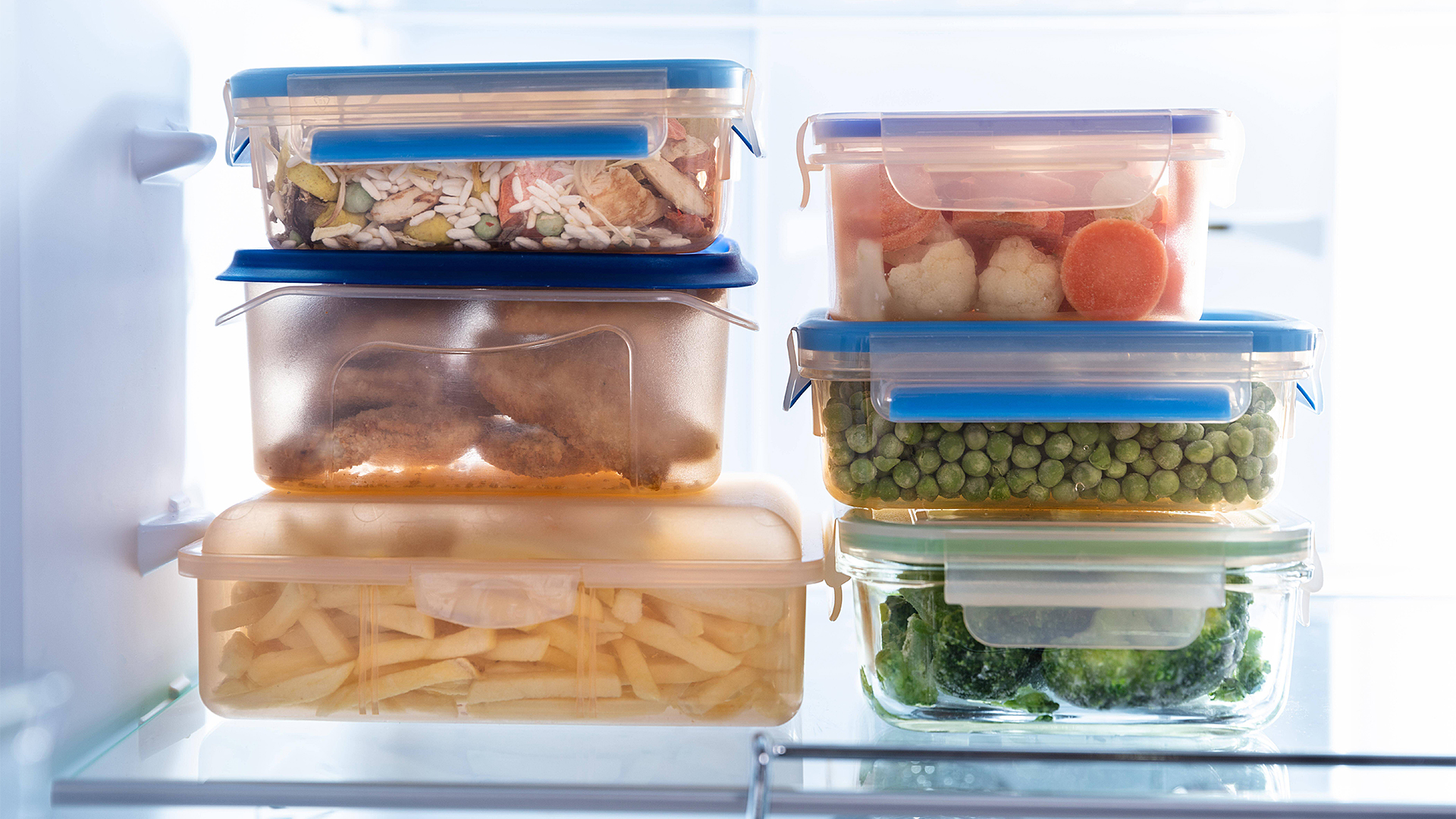 Mehrere Plastikdosen mit Lebensmitteln stehen in einem beleuchteten Kühlschrank.
